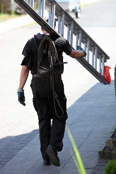 Chimney technician carrying ladder on shoulder to job site