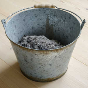 a metal bucket with a pile of fireplace ash inside